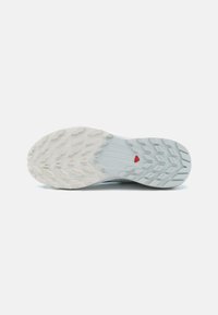 Semelle de chaussure de sport avec un design en caoutchouc blanc texturé, dotée d'un accent bleu et d'un motif de traction multidirectionnelle pour une adhérence améliorée.