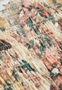 Nahaufnahme von gerafftem Stoff mit einem floralen Muster in gedämpften Rosa-, Grün- und Cremetönen, versehen mit stoffbezogenen Knöpfen.