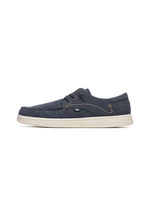 Zapatos de lona azul marino para hombre con acabado texturizado, suela de goma blanca y costuras marrones; cuentan con tres ojales y un detalle con el logo de la marca.