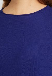 Niebieski sweter z okrągłym dekoltem, gładką fakturą i delikatnym prążkowaniem. Zbliżenie ukazuje szczegóły tkaniny i wyrazistość szwów.