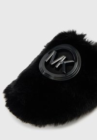 Ciabatta nera in soffice peluche con un logo circolare nero in rilievo che presenta le lettere "MK" sulla parte anteriore.