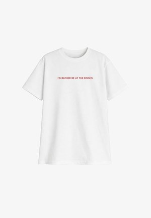 Camiseta blanca de manga corta con texto rojo centrado en el frente que dice "PREFERIRÍA ESTAR EN EL RODEO."