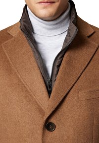 Brązowy płaszcz z wełny z dopasowanym kołnierzem, posiadający szary, zapinany na zamek wewnętrzny oraz zapięcie na guziki. Gładka tekstura z dopasowanym krojem.