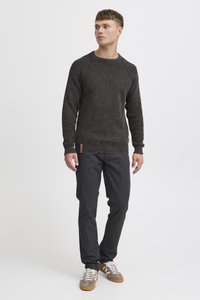 Mørk strikket sweater med tekstureret m�ønster, ribbede manchetter og kant. Kombineret med mørke bukser og afslappede grå-brune sneakers.
