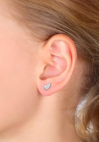 Orecchino a perno a forma di ala argentata con dettagli rigati. Realizzato in metallo, presenta una superficie liscia e riflettente e un design minimalista.