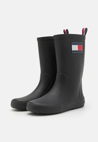 Bottes de pluie en caoutchouc noir au design épuré, avec des semelles texturées et un écusson affichant des rayures bleu, rouge et blanc sur le côté.