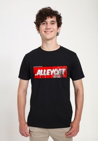 Černé bavlněné tričko s velkým červeným grafickým prvkem a bílým textem " .ALLEYCAT. " na přední straně, s texturovaným, stříkaným efektem.