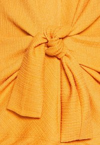 Tejido texturizado naranja con un diseño anudado en el centro, que presenta sutiles estrías verticales y una apariencia suave y ligera.