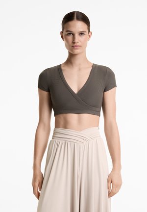 Olivgröna ribbade crop top med korta ärmar och djup V-ringning, tillsammans med en beige, högmidjad plisserad kjol. Släta tygtexturer.