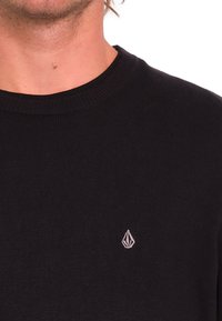 Maglione nero in maglia con una texture a coste e scollatura girocollo. Presenta un piccolo logo ricamato sul lato sinistro vicino al petto.