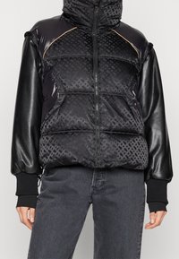 Czarna kurtka puchowa z wysokim kołnierzem, pikowanym wzorem, błyszczącym materiałem na górze oraz rękawami o strukturze skóry. Mankiety ściągane na dzianinę i zamek błyskawiczny z przodu.
