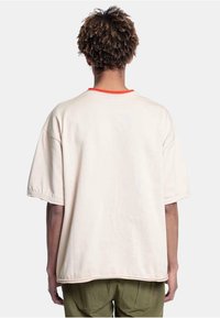 Crèmefarget oversized t-skjorte med korte ermer, rund utringning med røde detaljer og rett avskjæring, vist bakfra.