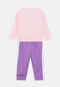 Pink sweatshirt with white stripes on sleeves and purple sweatpants featuring white side panels. Soft fabric with elastic cuffs.