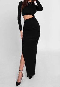 Musta pitkähihaista mekkoa, jossa on leikattu kohta rinnan alla. Mekko on muotoiltu tiukasti, siinä on reiden ylle ulottuva halkio, sileä pinta ja tyylikkäästi suunniteltu ilme.