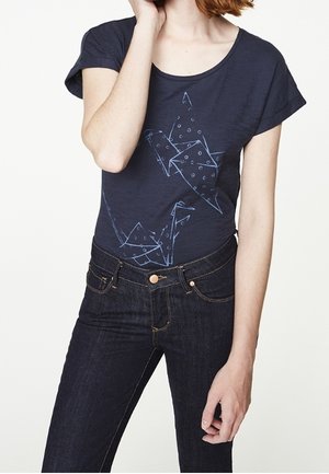 T-shirt bleu marine à manches courtes avec un motif grue origami bleu clair. Associé à un jean en denim foncé et une coupe classique.