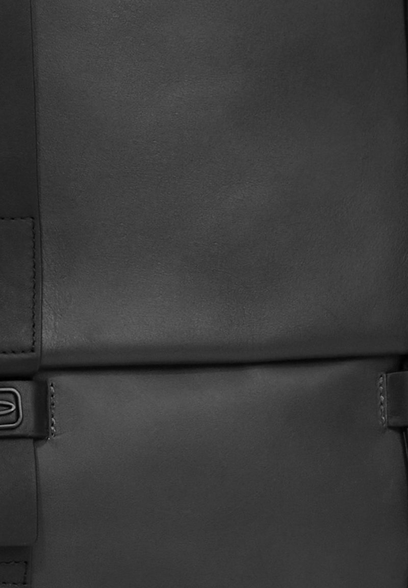 Sac en cuir noir avec une texture lisse, comportant un pli central, du matériel pour la sangle latérale et un design minimaliste. Aucun motif ou accent visible.