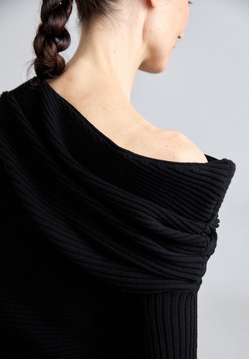 Haut noir à côtes avec un design décolleté, présentant une texture de tissu doux, drapé et des plis superposés le long de l'encolure et du dos.