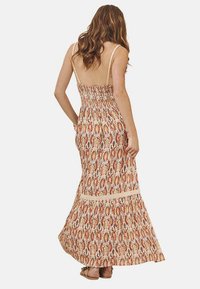 Vestido maxi con espalda fruncida, tirantes finos y una tela estampada y colorida con tonos rojos y amarillos; con un borde de encaje en el dobladillo.