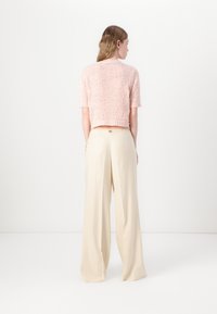 Lys rosa strikket kortermet genser med en cropped design, kombinert med beige vidde bukser med lommer og en subtil logodetalj.