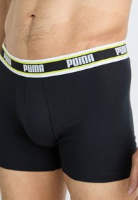 Fekete boxer alsónadrág puha anyagból. Kontrasztos derékpánttal rendelkezik, amelyen fehér és sárga árnyalatú "PUMA" logo található. Sima textúra.
