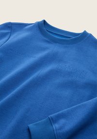 Felpa blu realizzata in un morbido tessuto, con scollatura e polsini a costine. Logo testurizzato e scritta motivazionale stampata sulla parte anteriore.
