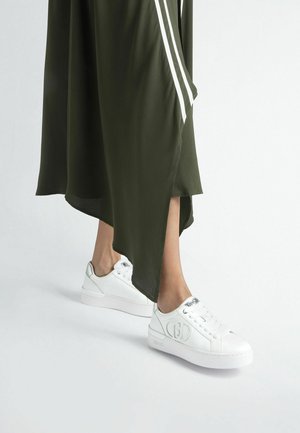 Sneakers bianchi in pelle liscia, dotati di occhielli e di un dettaglio con logo. Abbinati a un vestito verde oliva con strisce laterali bianche.