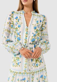 Floral dress with long sleeves, white fabric featuring blue flowers and green leaves, tied waist, v-neckline, and decorative buttons.