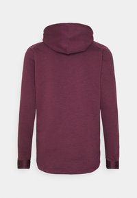 Sudadera con capucha en burdeos intenso, tejido suave, con mangas largas y puños contrastantes. Presenta un diseño simple y sin adornos en la parte trasera.