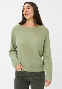 Maglione verde a maglia con scollo ampio, maniche lunghe e polsini a costine. Abbinato a pantaloni in velluto a coste verde scuro.