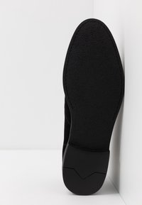Semelle de chaussure noire avec une surface texturée et un design angulaire. La semelle a un bord lisse et présente une légère courbure au niveau de l'orteil.
