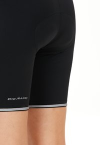 Svarta sportshorts med en åtsittande design, slät textur och reflexgrå detaljer vid fållen. Varumärket heter "ENDURANCE."