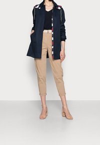 Manteau trench marine avec col à motifs, pantalon beige coupé, et sandales à talons carrés couleur nude. Design minimaliste avec poches fonctionnelles.