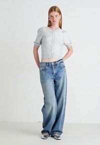 Grijs, aangeknippt button-up sweater met korte pofmouwen, gecombineerd met lichtblauwe wijdvallende jeans met een verouderd uiterlijk en een ontspannen pasvorm.