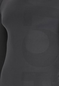 Nahaufnahme eines schwarzen, enganliegenden Hemdes mit einem großen, dezenten Muster der Zahl 5 in unterschiedlichen Stricktexturen auf dem Stoff.