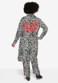Zebra-muster Outfit mit langen Ärmeln, verfügt über den auffälligen roten Text "WILD & FREE" auf dem Rücken. Lockerer Schnitt, aus weichem Stoff, mit seitlichen Akzenten.