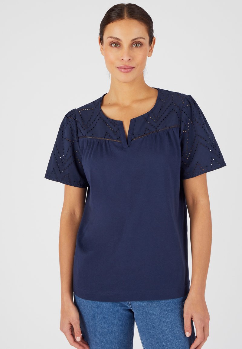 Top en coton bleu marine avec des manches courtes ornées de détails en œillets formant un motif géométrique et un décolleté à fente à l'avant. Coupe traditionnelle.