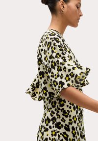Bloemenpatroon jurk in lichte kleuren met zwarte en gele accenten. Heeft korte, gerimpelde mouwen en een nauwsluitende silhoutte. Zachte textuur.