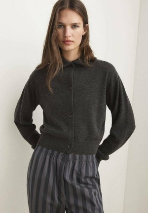Cardigan tricoté gris foncé avec un devant à boutons et un col classique, associé à un pantalon gris à rayures avec une taille élastique.
