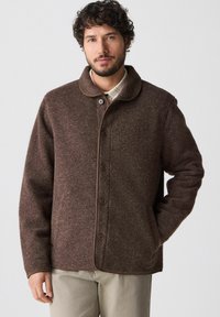 Brauner Wollmantel mit rundem Kragen, Knopfverschluss und seitlichen Taschen. Verfügt über eine strukturierte Oberfläche und kontrastierende Besätze an den Kanten.