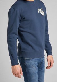 Marinblå crewneck sweatshirt i mjukt tyg. Har en vit tryckt grafik "CAN'T BUST 'EM" på bröstet. Ribbstickade ärmslut och nederkant.