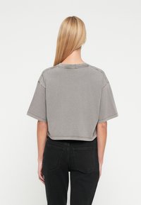 Κοντομάνικο γκρι μπλουζάκι κομμένο, με στρογγυλή λαιμόκοψη και ορατές ραφές, συνδυασμένο με μαύρο τζιν. Μαλακό βαμβακερό ύφασμα.