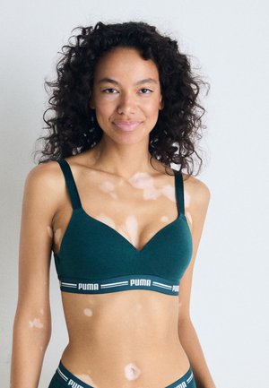 Green fabric bra with a v-neck design, adjustable straps, and a contrasting black band featuring white "PUMA" logo. Smooth texture, simple style.