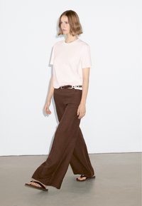 Light pink t-shirt, brown wide-leg pants, brown belt with silver accents, and black flip-flops. Simple design, smooth textures, casual look.
