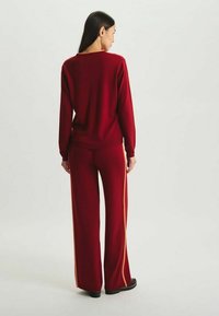 Pull en tricot rouge et pantalon ample assorti avec des rayures latérales orange. Texture douce et coupe décontractée, conçu pour un port décontracté.