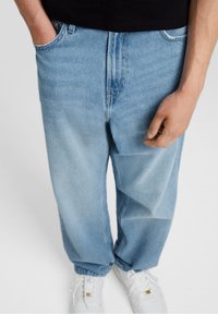Ljust blå denimjeans med lös passform, framfickor och synlig söm. Kombineras med vita sneakers, som visar upp en avslappnad stil.
