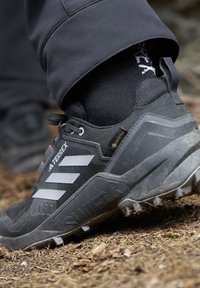 Czarne buty trekkingowe z szarymi paskami i wytrzymałą podeszwą, z teksturowaną cholewką i logo GORE-TEX. Nosi się je z czarnymi skarpetami.