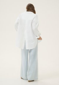 White oversized shirt with a back slit design, paired with light blue wide-leg denim pants. Smooth fabric and relaxed fit.