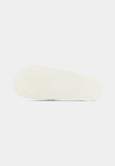 Semelle de chaussure en caoutchouc blanc avec un motif hexagonal et des lignes de grip texturées. Surface lisse avec un léger éclat, incurvée au niveau des orteils.