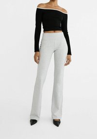 Zwarte geribbelde off-shoulder top met lange mouwen, gecombineerd met lichtgrijze flared broek; beide van zachte, rekbare stof. Zwarte puntige hakken.