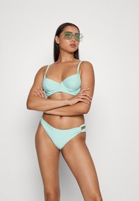 Um biquíni verde menta claro com tecido texturizado; a parte de cima tem copas com aro, alças ajustáveis, e a parte de baixo tem detalhes recortados.